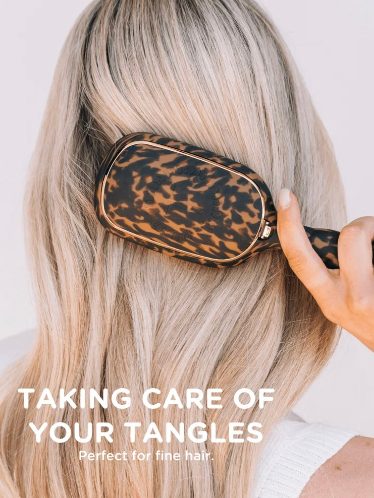 A close-up of a person with long blonde hair using a leopard-print hairbrush to detangle their hair. White text at the bottom reads 'TAKING CARE OF YOUR TANGLES' and 'Perfect for fine hair.