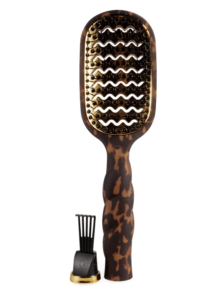 A tortoiseshell hairbrush with a wavy gold-tone metal bristle head and a matching black-and-gold stand, shown on a plain white background.
