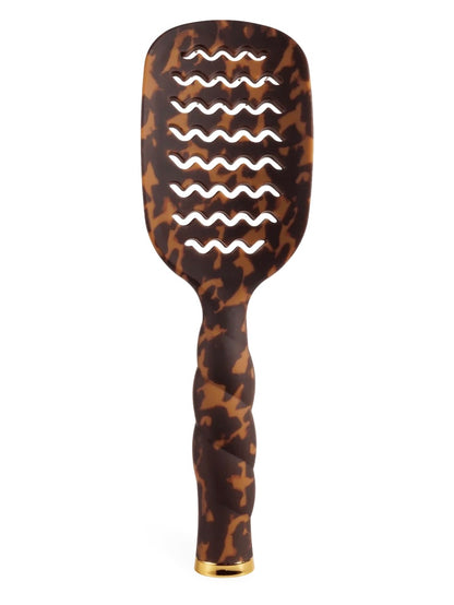 A hairbrush with a brown and black tortoiseshell pattern, featuring wavy cutouts on the brush head and a twisted handle with a gold-colored end cap, set against a plain white background.