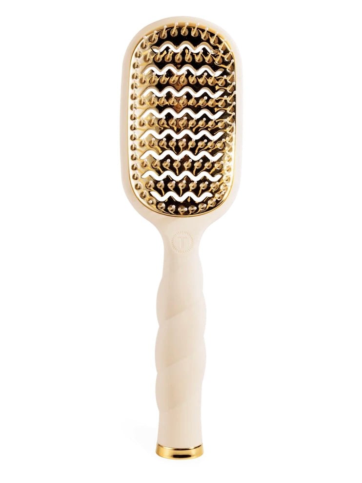 An oval-shaped hairbrush with a cream-colored handle and a gold-toned metal head featuring textured, raised nubs, shown on a solid white background.