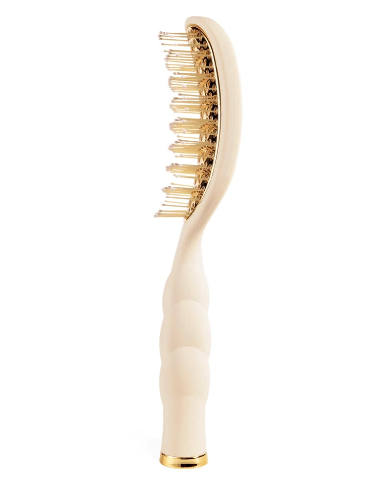 A luxury hairbrush with a sculpted cream handle and a gold-toned oval head, shown against a solid white background.
