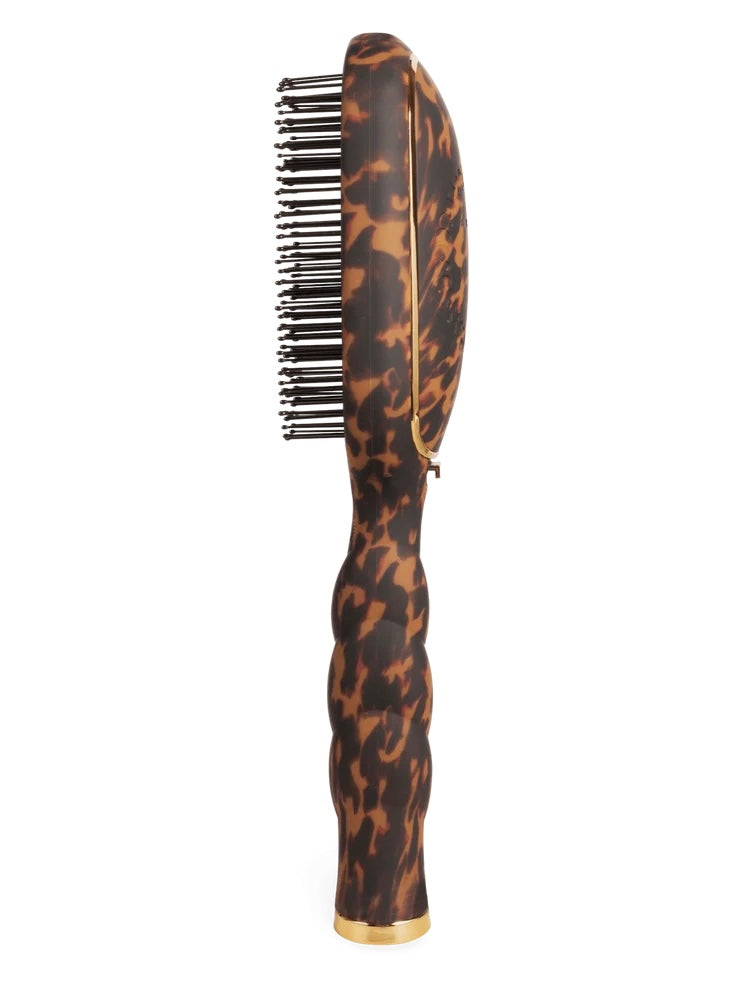 A hairbrush with a glossy tortoiseshell pattern handle and black bristles, featuring gold trim and a gold base accent, shown against a plain white background.