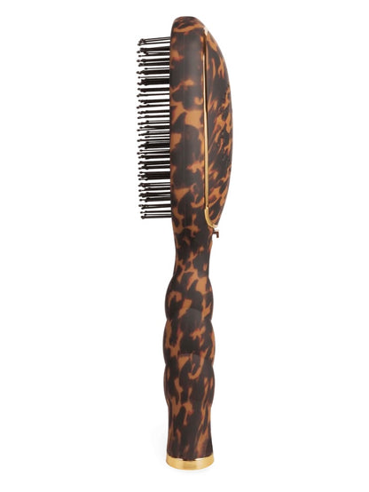 A hairbrush with a glossy tortoiseshell pattern handle and black bristles, featuring gold trim and a gold base accent, shown against a plain white background.