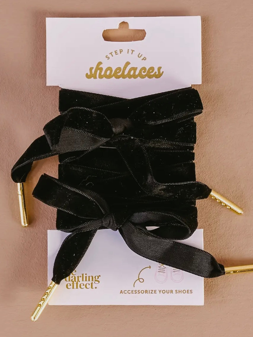 Black shoelaces with gold tips on a ' Darling Effect' card against a beige background