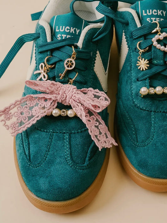 Teal sneakers with decorative laces and charms on a beige background