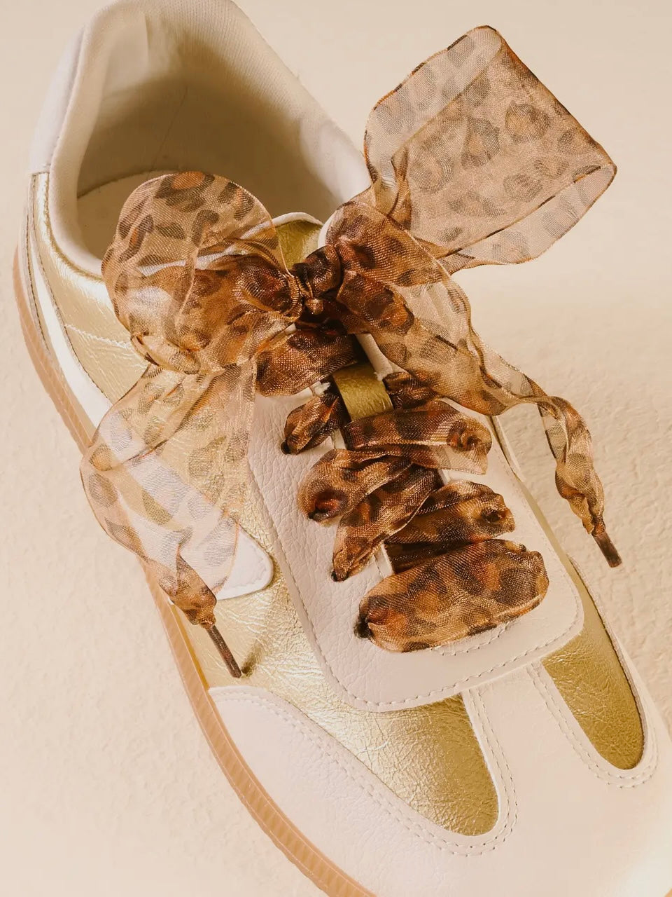 White sneaker with a large leopard print bow on a beige background
