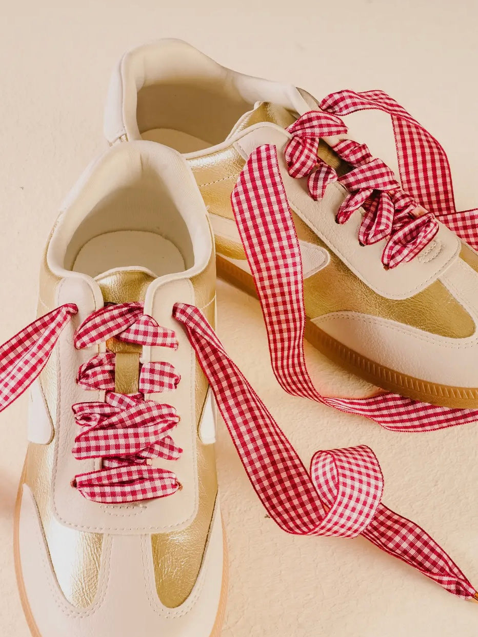 White sneakers with red gingham shoelaces on a beige background